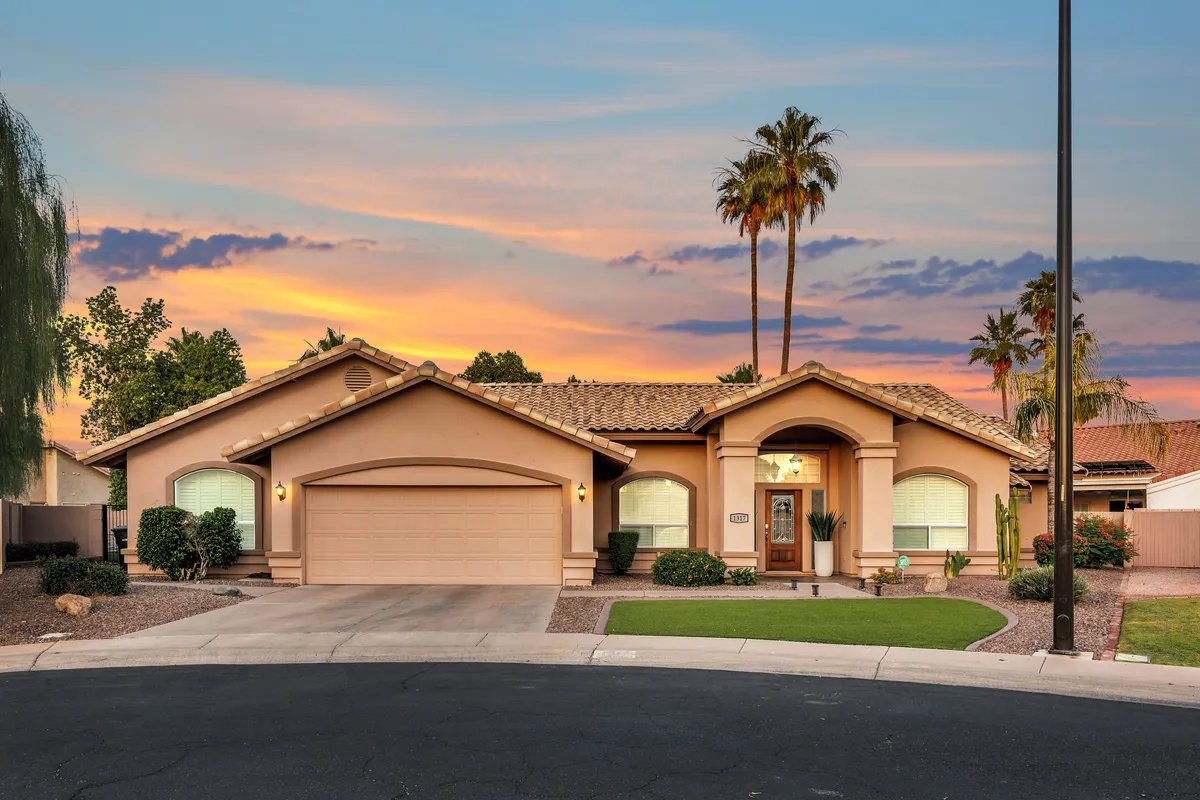 A beautifully landscaped front entrance featuring lush greenery, palm trees, and a soft sunset sky. The porch invites moments of relaxation, family gatherings, or simply enjoying the Arizona evening outdoors.