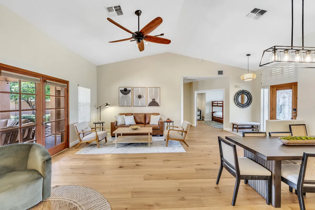 A welcoming living and dining area featuring a large wooden table, comfortable seating, and contemporary decor. Sunlight streams through the windows, illuminating a versatile space perfect for group meals, meetings, or casual conversations.