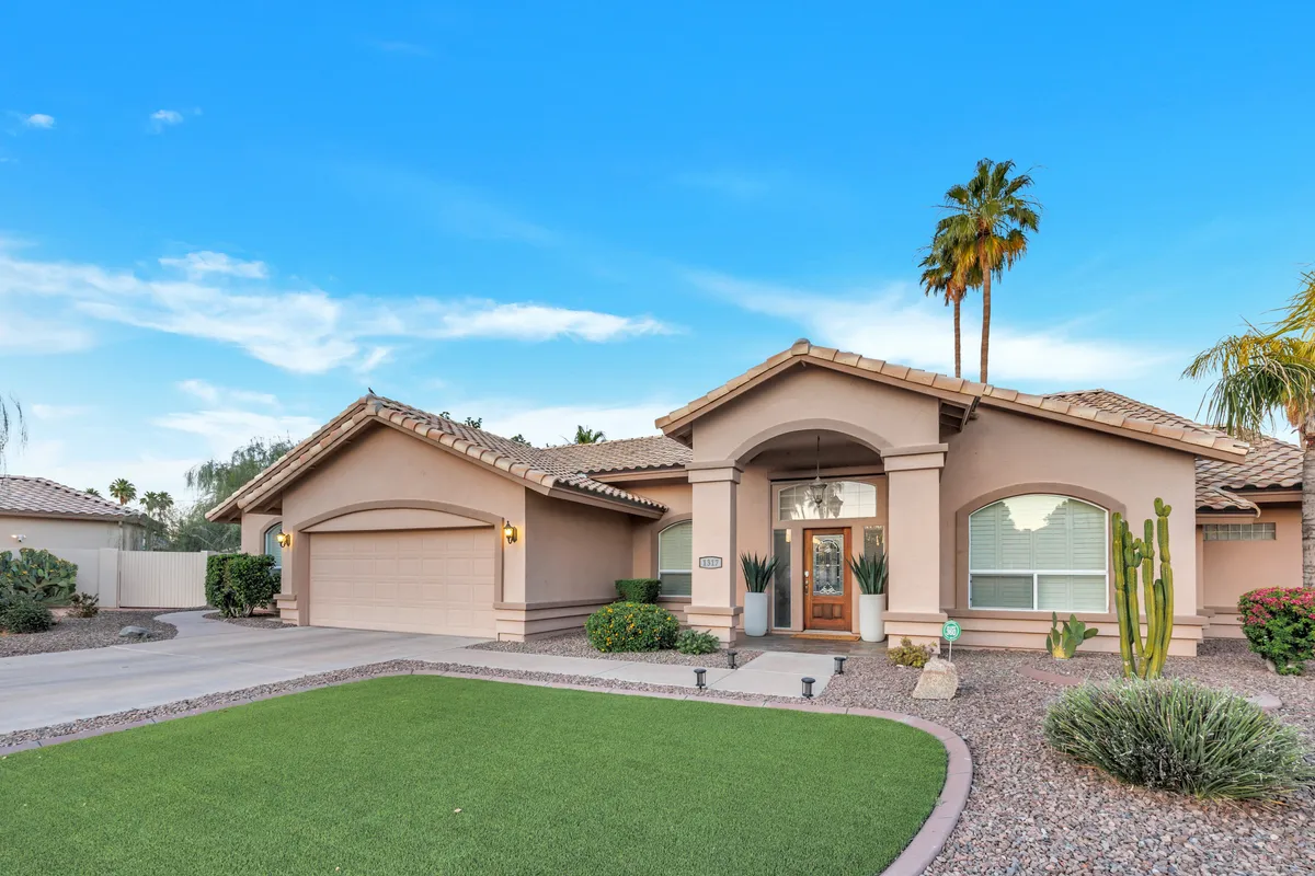 An inviting front yard with manicured landscaping, tall palm trees, and a welcoming entryway. The garage and spacious driveway can be seen, evoking the feeling of arriving home to a relaxing, family-friendly environment.