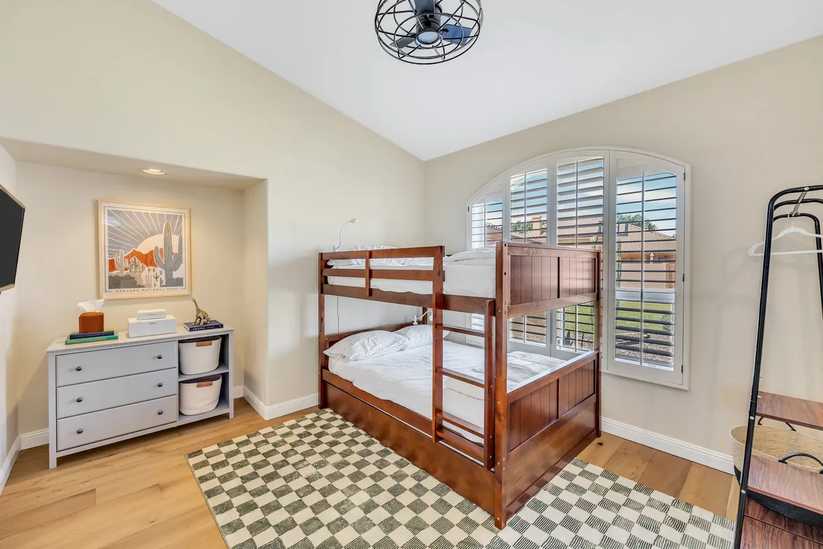 A playful yet cozy bedroom featuring a bunk bed, cheerful artwork on the wall, and a window with shutters. The space invites both relaxation and imaginative play, making it ideal for children or family groups.