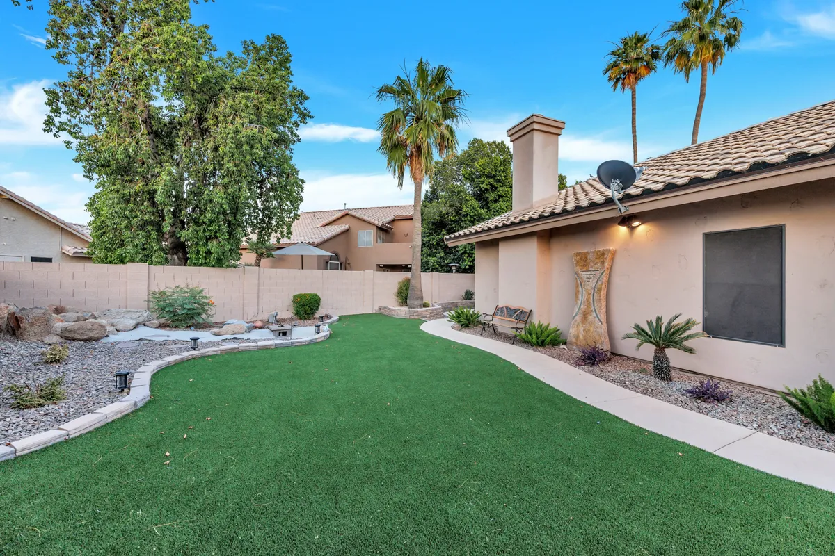 Expansive, lush green lawn accented by decorative rocks, palm trees, and a cozy bench. The fenced yard offers ample play space for kids and pets, with peaceful nooks for relaxation and easy supervision.