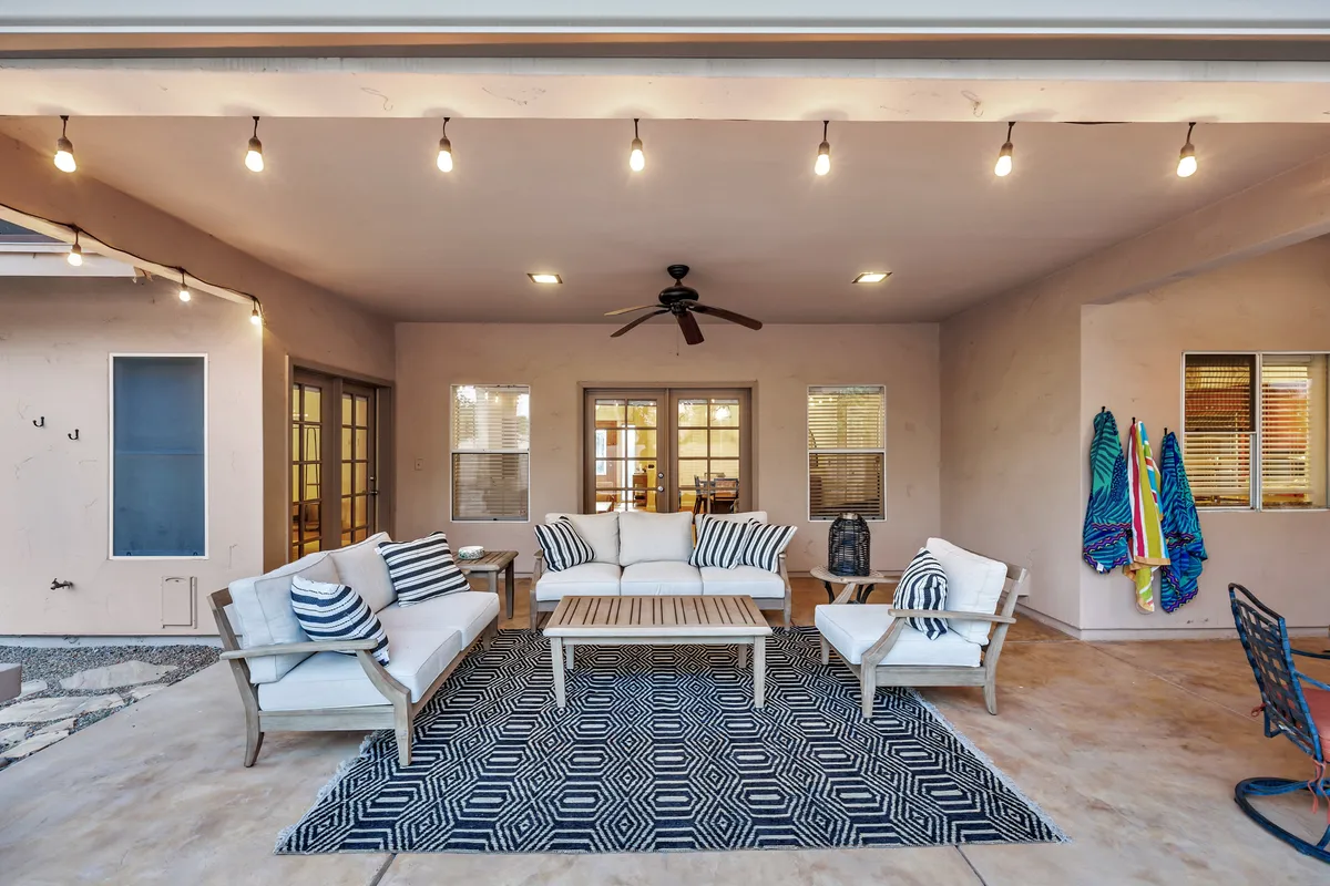 A stylish living room with a comfortable sofa seating arrangement, a modern coffee table, and decorative hanging lights. The space is bathed in natural light, creating a casual and welcoming atmosphere perfect for relaxation, reading, or remote work. The room’s open design hints at connectivity between indoor and outdoor living.
