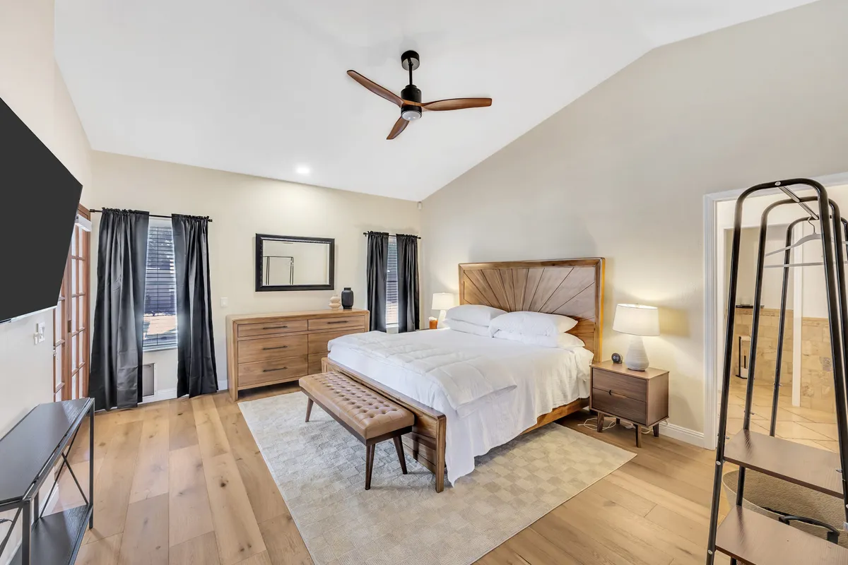 A serene bedroom centered around a comfortable bed flanked by nightstands, with a wooden dresser and mirror providing ample storage. The mood is restful, and the space is brightened by natural light.