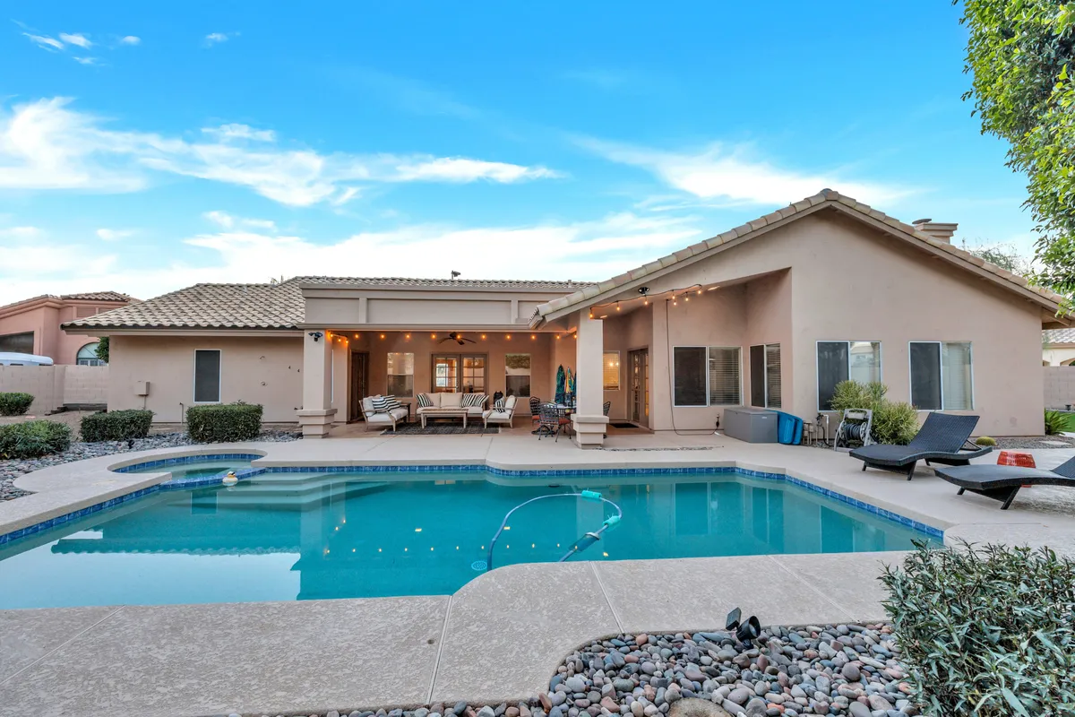 A view of the home's inviting backyard featuring a sparkling swimming pool, ample outdoor seating, and a shaded patio area. The setting is relaxed with soft lighting, suggesting the perfect environment for after-hours networking or unwinding after a productive day.